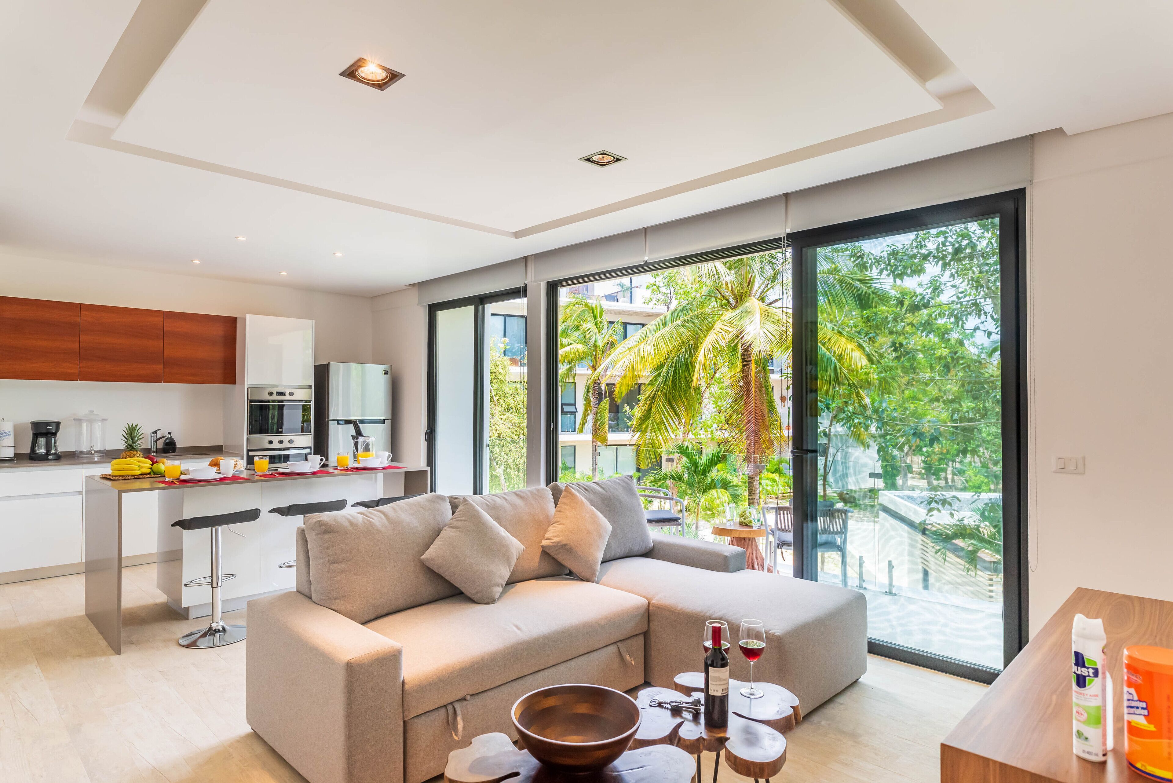Sala de estar moderna com sofá, mesa de centro e vista para uma varanda com palmeiras.