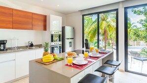 A modern kitchen with a central island, stainless steel appliances, and a large window with a view of palm trees. - Panoramic By Alegria Rentals and Sandy Powerful  (Tulum)
