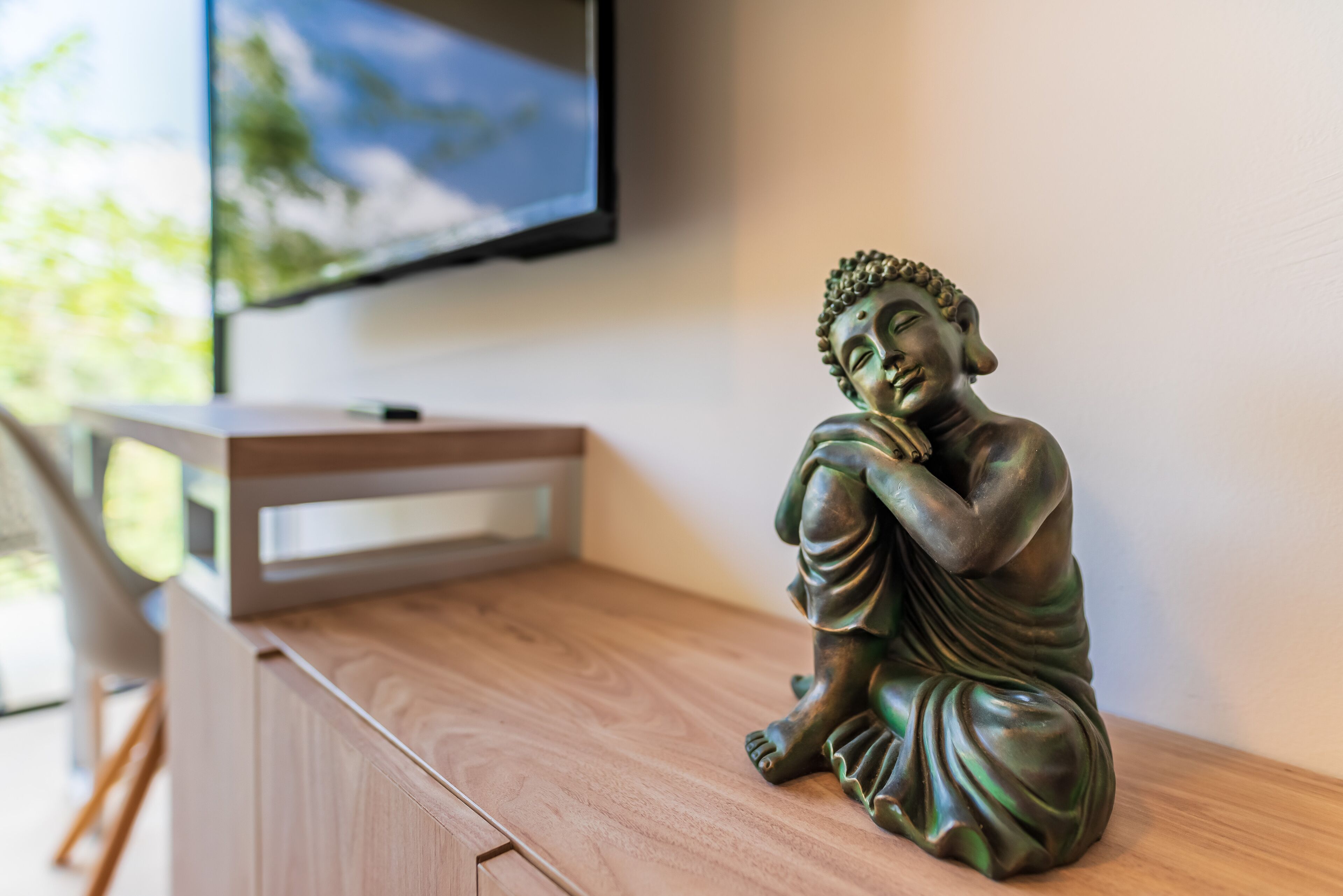 Une statue de Bouddha sur une surface en bois, avec un téléviseur fixé au mur en arrière-plan.