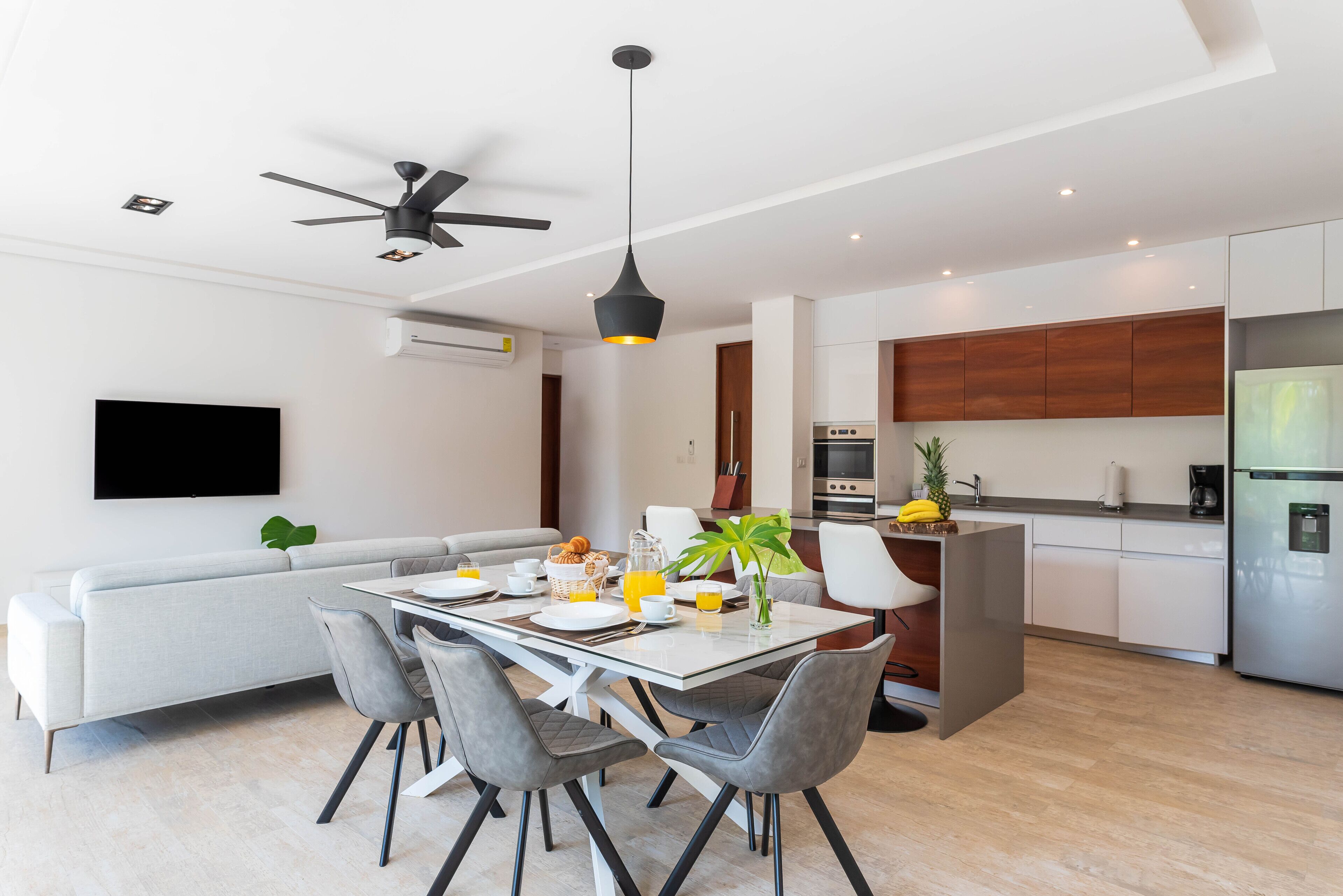 A modern kitchen with a built-in oven and refrigerator, a dining area with a table set for two, and a ceiling fan.