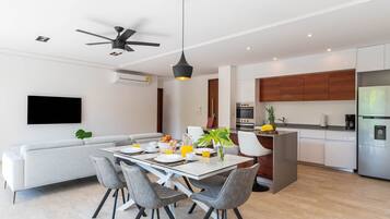 A modern kitchen with a built-in oven and refrigerator, a dining area with a table set for two, and a ceiling fan.