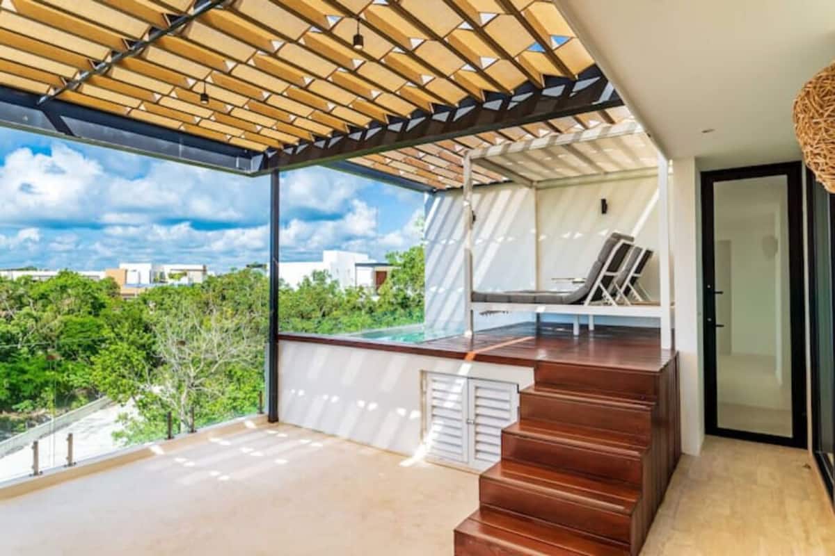 Varanda moderna ao ar livre com escadas de madeira, área de estar e vista para o verde e edifícios.