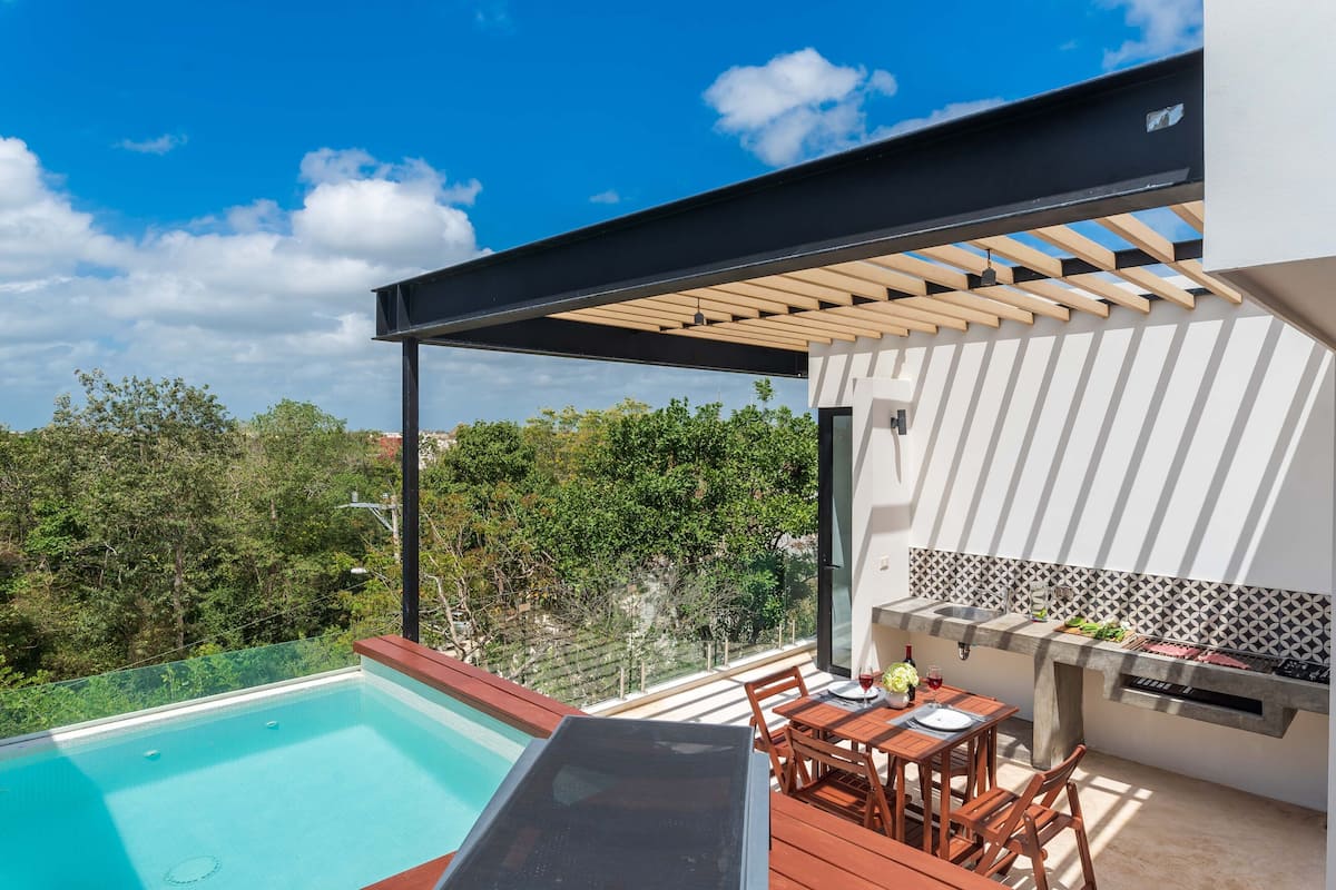 Um pátio moderno ao ar livre com piscina, deck de madeira e área de churrasqueira integrada.