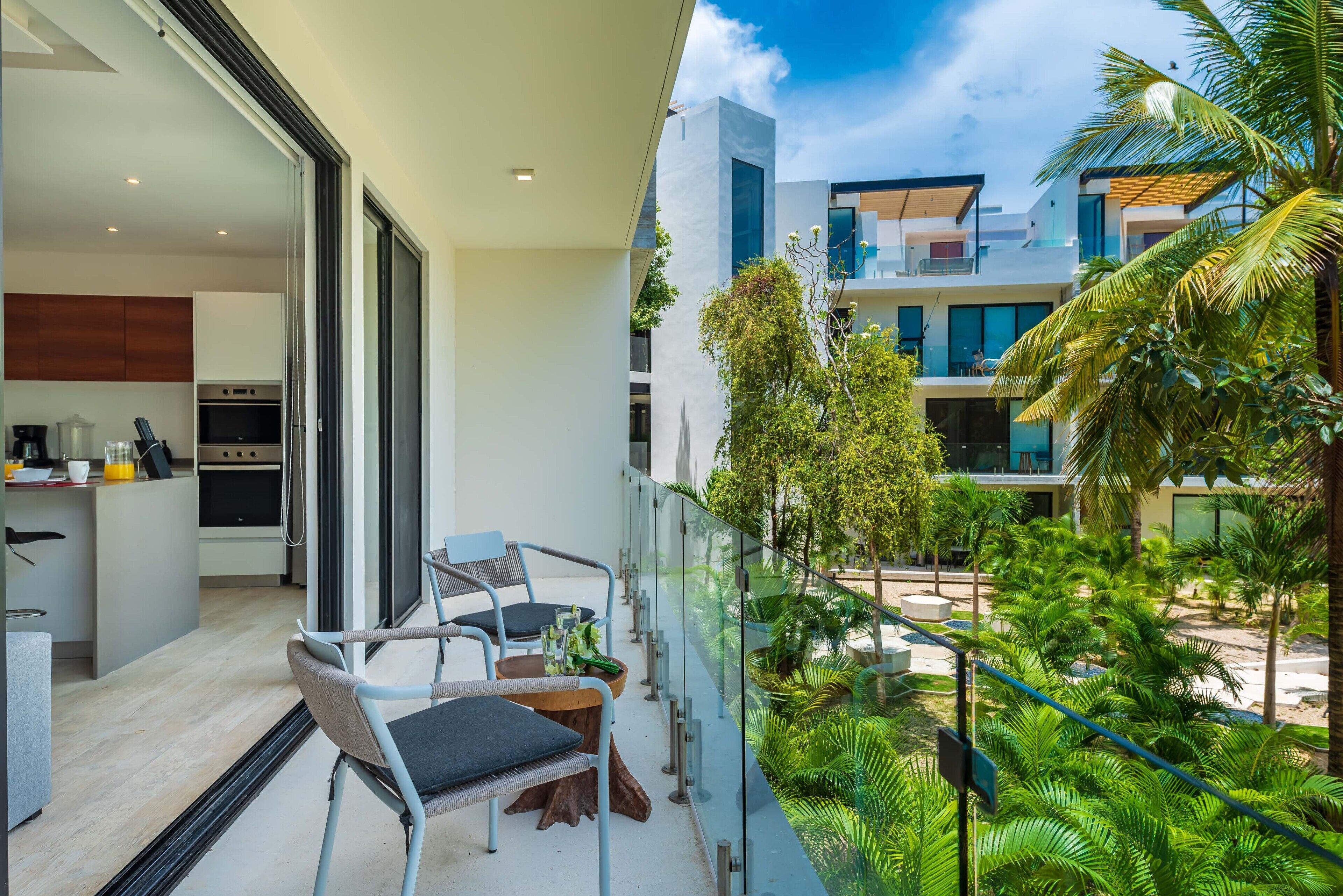 A balcony with a view of a modern building, a kitchen area, and a seating arrangement.