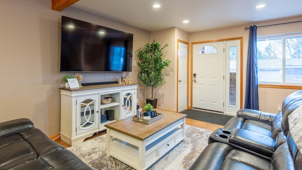 A living room with a flat-screen TV, a white entertainment unit, a coffee table, a black leather couch, and a door leading to another room. - Home sweet home! (Missoula)