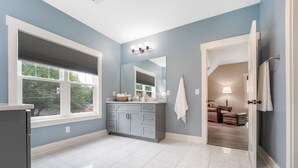 Une salle de bain moderne avec un meuble-lavabo gris, un grand miroir et une vue sur le salon par une porte ouverte.