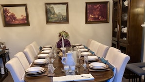 Un comedor formal con una gran mesa de madera dispuesta para ocho personas, rodeada de sillas blancas tapizadas.