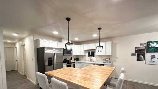 A modern kitchen with white cabinets, stainless steel appliances, and a wooden island with bar stools. - Prime location, Aurora viewing, Fast WI-FI!! (Fairbanks)