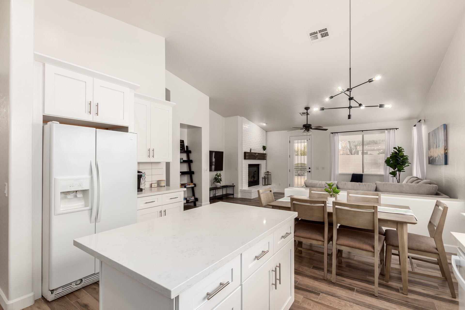 A modern kitchen with white cabinetry, a central island, and a dining area with wooden chairs and a table.