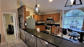 A modern kitchen with wooden cabinets, stainless steel appliances, and a black countertop. - Ultimate Heated Pool Retreat ★ Fire Pit + Game Room ★ Family Fun (Davenport)