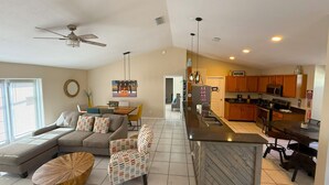 A spacious living room with a sofa, armchair, and coffee table, a kitchen with wooden cabinets and appliances, and a ceiling fan. - Ultimate Heated Pool Retreat ★ Fire Pit + Game Room ★ Family Fun (Davenport)