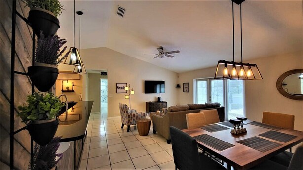 A modern living room with a dining area, a ceiling fan, and a TV mounted on the wall. - Ultimate Heated Pool Retreat ★ Fire Pit + Game Room ★ Family Fun (Davenport)