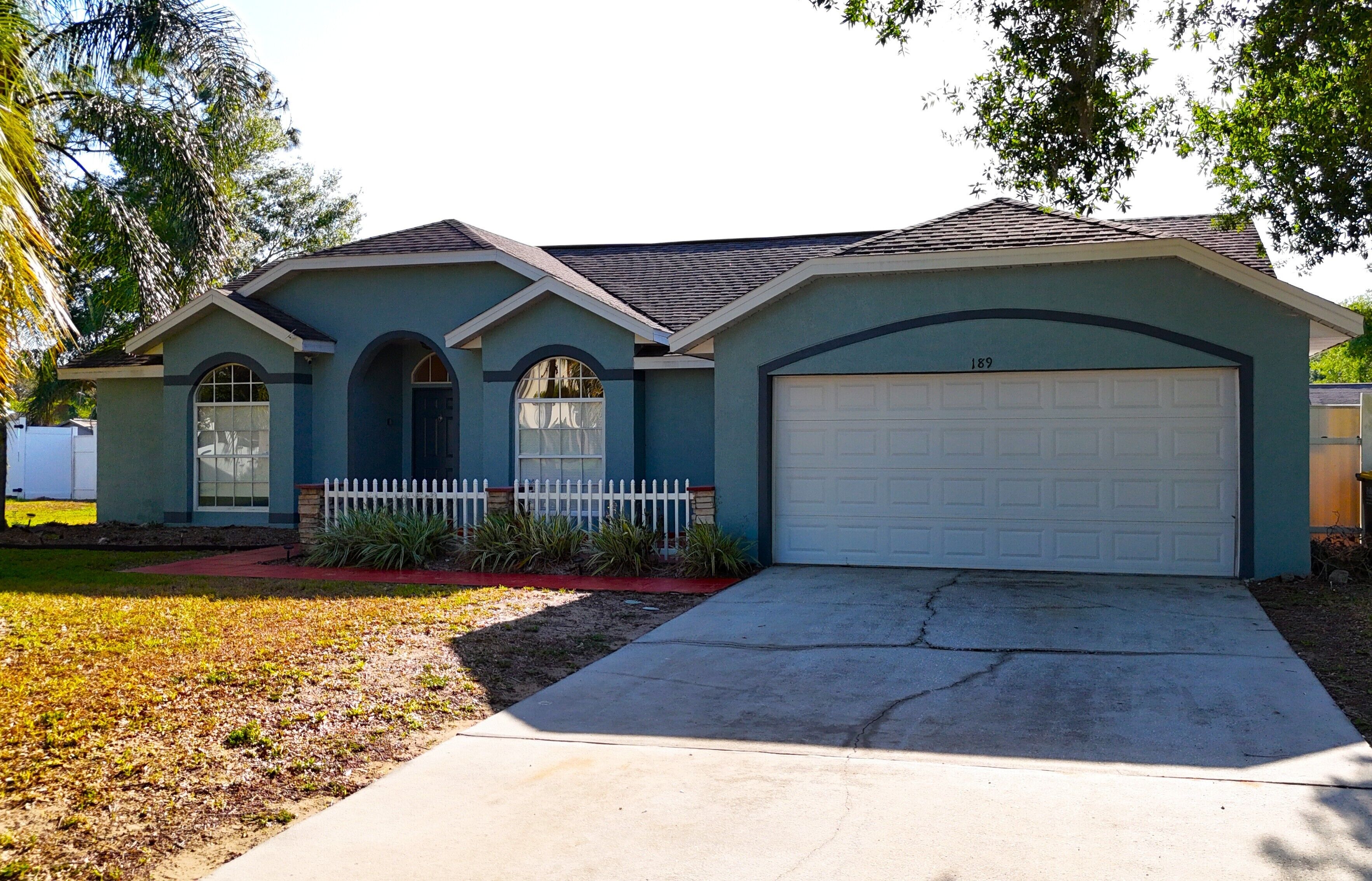 A single-story house with a garage, a front yard with a white picket fence, and a driveway.