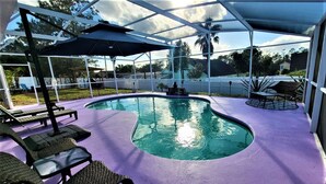 A covered outdoor swimming pool with lounge chairs and umbrellas, surrounded by a white fence and trees. - Ultimate Heated Pool Retreat ★ Fire Pit + Game Room ★ Family Fun (Davenport)