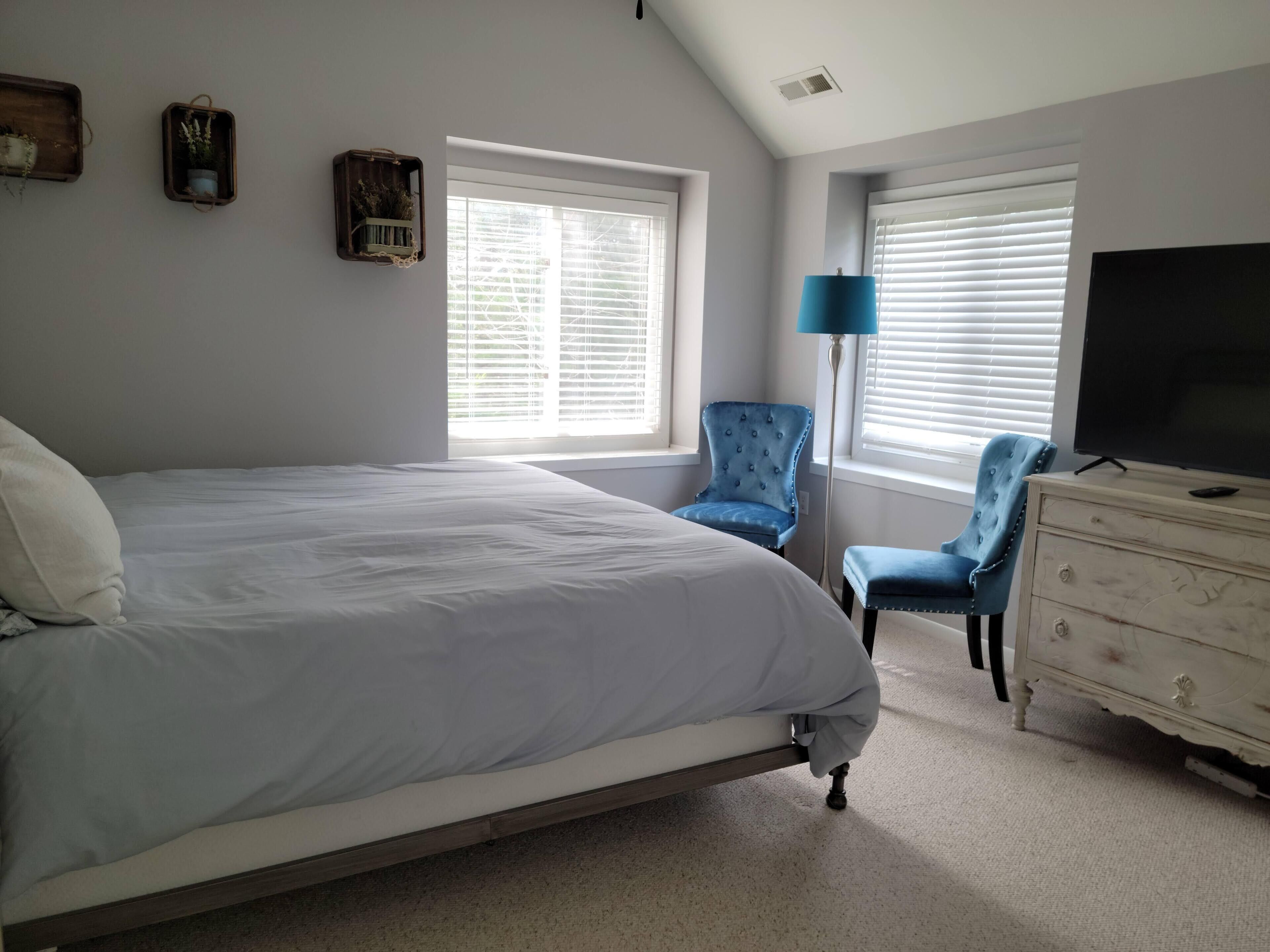 Une chambre à coucher avec un lit, deux chaises, une commode et un téléviseur.