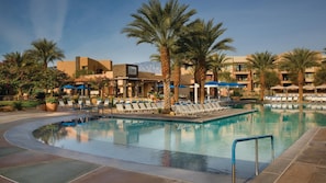 A pool area with lounge chairs and palm trees, surrounded by buildings with a desert architectural style.