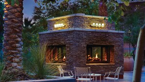 A stone-built outdoor fireplace with two large windows, surrounded by chairs and plants. - Marriott Shadow Ridge at Palm Desert, CA (Palm Desert)