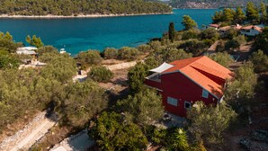 Une propriété située sur la côte, avec un bâtiment à toit rouge, une vue dégagée sur la mer et une végétation luxuriante tout autour.
