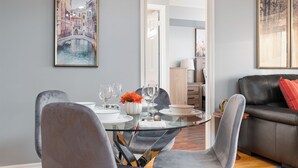 A dining area with a glass table, grey chairs, and a black leather sofa. - Duke Of York Boutique Suites (Mississauga)