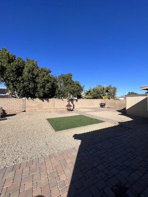 Relax in the serene patio area surrounded by lush trees and a brick wall, perfect for unwinding.