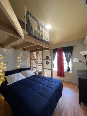 A bedroom with a bunk bed, a desk, a lamp, and fairy lights.