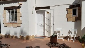 Un edificio blanco con una entrada protegida por una reja y una planta en maceta al frente.