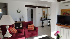 Una sala de estar con chimenea, sillones rojos, televisor y una zona de comedor con mesa y sillas.
