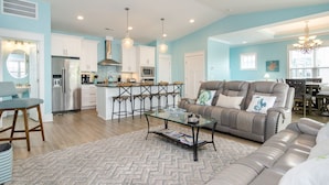 A modern kitchen with white cabinets, stainless steel appliances, and a central island. - Spacious 5 BR Home Across from Beach! (Kure Beach)
