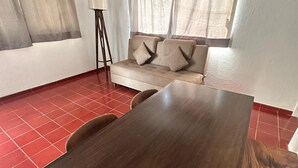 Una habitación con una mesa de comedor de madera, un sofá beige con cojines y una lámpara de pie.
