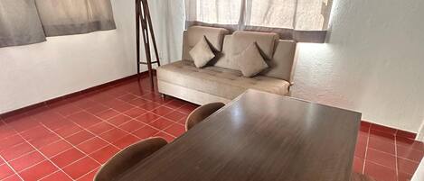 A room with a wooden dining table, a beige sofa with cushions, and a floor lamp.