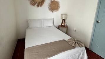 A bedroom with a bed, a ceiling fan, two wall-mounted decorative items, a bedside lamp, and a door.