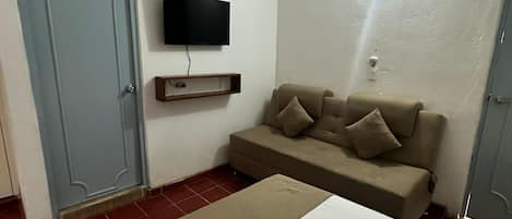 Ein Zimmer mit einem Bett, einem Sofa, einem an der Wand montierten Fernseher und einem Deckenventilator.
