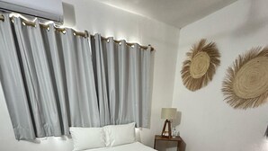 Una habitación de hotel con una cama, cortinas, una mesita de noche con lámpara y decoración en la pared.