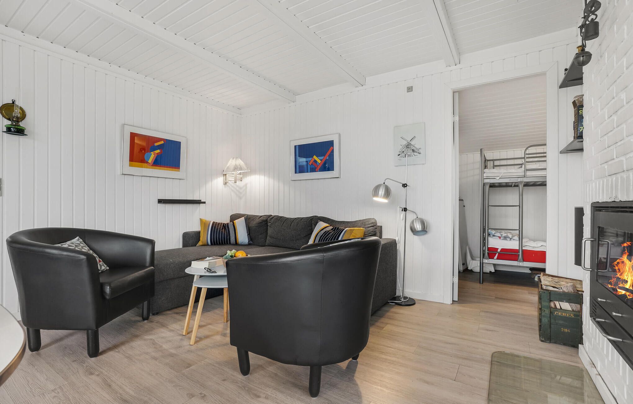 Un salon moderne comprenant un canapé, deux fauteuils, une table basse et une cheminée. Deux tableaux abstraits encadrés ornent le mur, ainsi qu’une table d’appoint avec une lampe et un porte-manteau.
