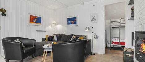 Un salon moderne comprenant un canapé, deux fauteuils, une table basse et une cheminée. Deux tableaux abstraits encadrés ornent le mur, ainsi qu’une table d’appoint avec une lampe et un porte-manteau.