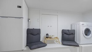 Une petite buanderie comprenant un lave-linge, deux chaises, une petite table avec des bougies et un réfrigérateur.