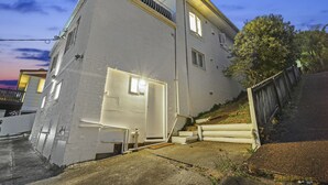 Une maison blanche à deux étages, avec une porte, des fenêtres et un petit balcon bien visibles.