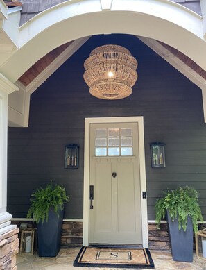 A dark grey house with a white door, two potted ferns, a wicker chandelier, and a stone staircase. - Beautiful lakefront property in Reynolds Lake Oconee. (Greensboro)