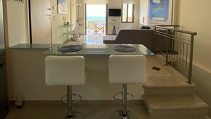 Una cocina moderna con una isla de cristal, dos taburetes de bar, una escalera y vistas al mar.