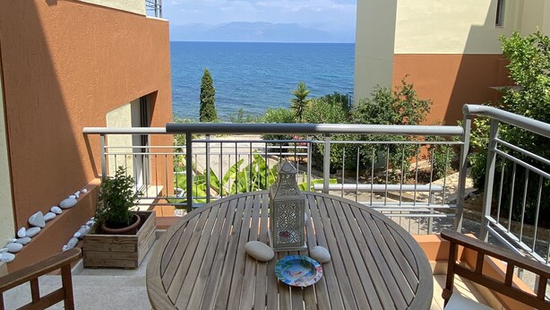 Una mesa y sillas de madera en un balcón con vista al mar.