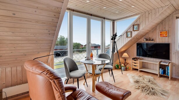 Una sala de estar moderna con paredes de madera, un televisor grande y un comedor con mesa y sillas.