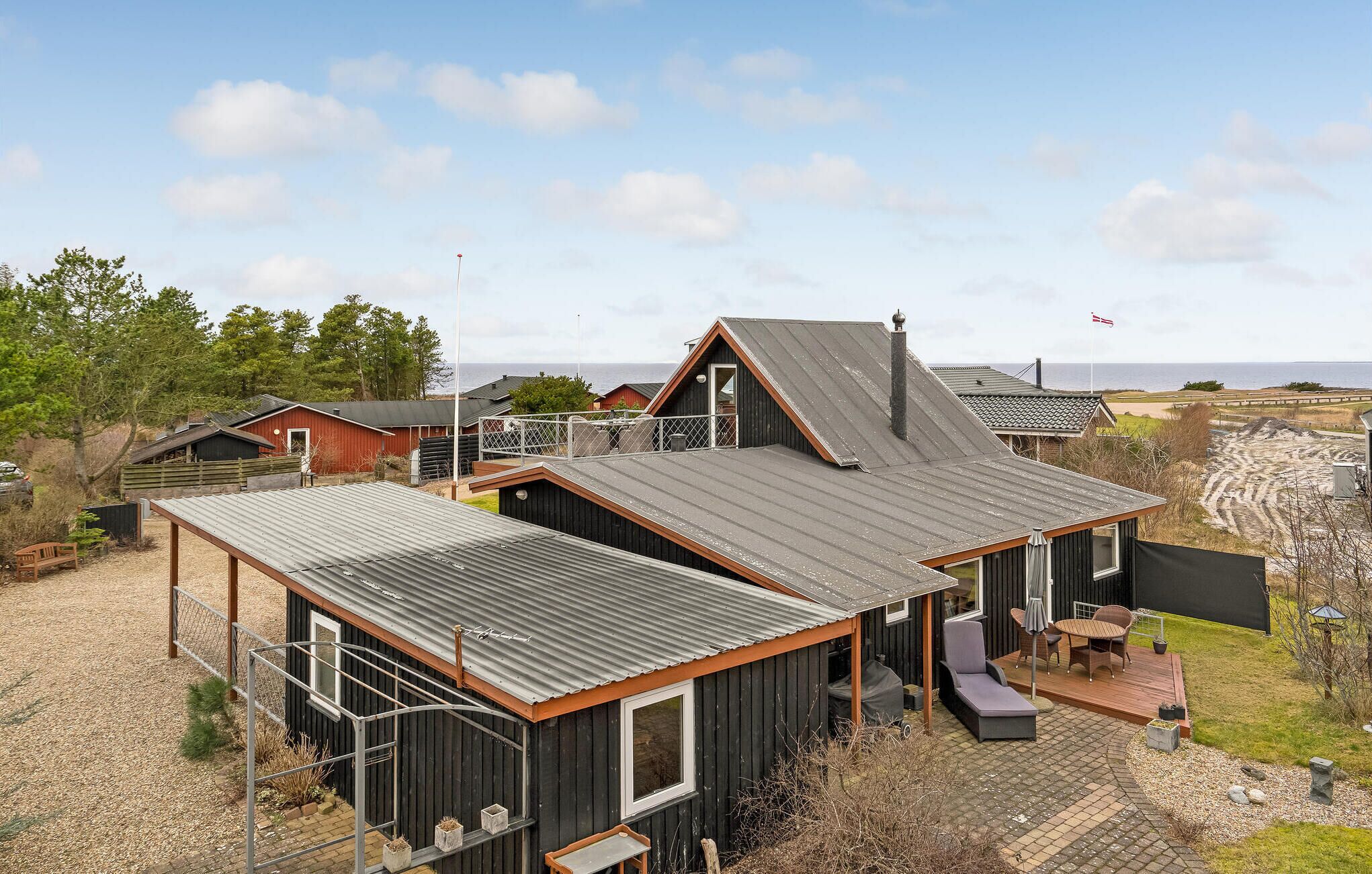 Ein modernes Haus mit einer großen Terrasse, einem überdachten Sitzbereich und Blick auf das Meer.