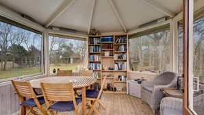 Un patio techado con una mesa y sillas de madera, un sofá de mimbre y una estantería llena de libros.
