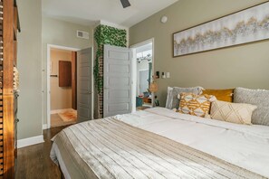 A bedroom with a large bed, a door leading to another room, and a wall-mounted artwork.