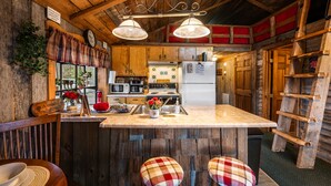 A rustic kitchen with wooden walls, a central island, bar stools, and a ladder shelf. - AUTHENTIC, Rustic, Cute, Cozy and close to everything! Real Cabin in the woods! (Pigeon Forge)