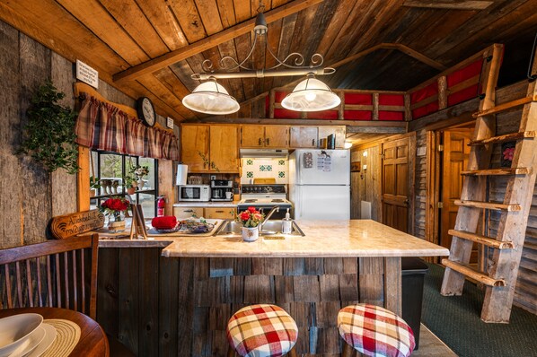 A rustic kitchen with wooden walls, a central island, bar stools, and a ladder shelf.