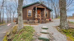 A rustic cabin with a wooden exterior, a porch with steps, and a gravel driveway surrounded by trees. - AUTHENTIC, Rustic, Cute, Cozy and close to everything! Real Cabin in the woods! (Pigeon Forge)