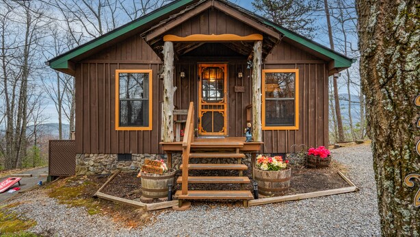 A rustic cabin with a wooden exterior, stone foundation, and a porch with steps leading to the entrance. - AUTHENTIC, Rustic, Cute, Cozy and close to everything! Real Cabin in the woods! (Pigeon Forge)