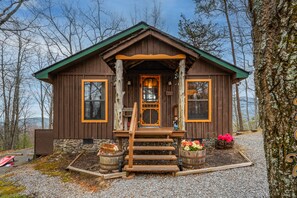 A rustic cabin with a wooden exterior, stone foundation, and a porch with steps leading to the entrance.