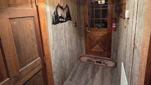 Un couloir intérieur en bois, avec une porte, un luminaire fixé au mur et un extincteur.
